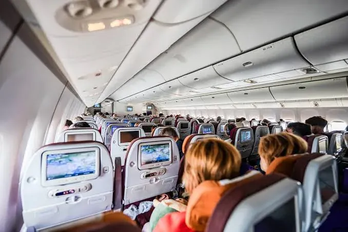 The cabin of an airliner mid-flight, seatbacks and screens receding down the aisle.