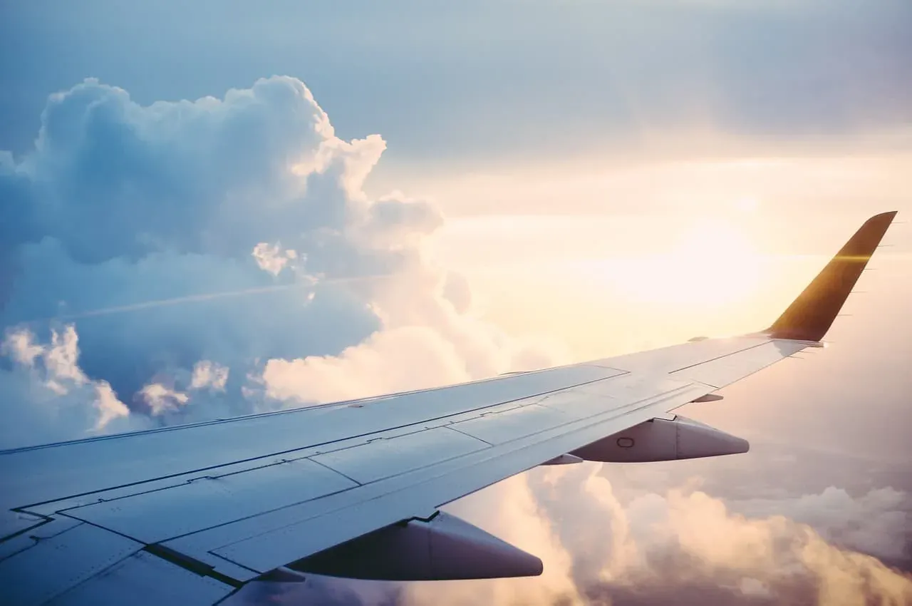An airliner's wing above a bank of clouds at cruising altitude, sunlight catching the winglet.