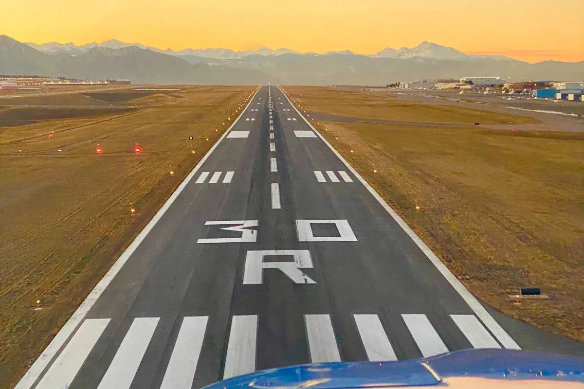 The view down a runway on approach, the large painted marking 30R in the foreground and mountains beyond.